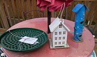 All three items: green seed catcher, white house feeder, blue tube feeder on table