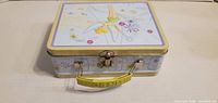 Top and side view showing lid artwork, side graphics, clasp, handle attachment