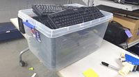 Clear tote on table filled with multiple black wired keyboards
