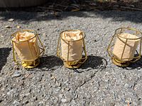 Three brass-plated geometric votive holders side by side on pavement