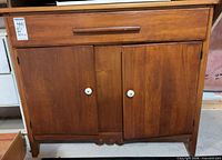 Front view closed showing drawer, two doors, knobs, feet
