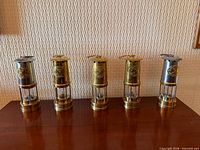 Five miners’ lamps lined up on table
