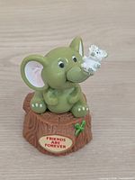 Front view of elephant figurine on stump showing plaque and flowers