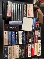 Overview of open box showing majority of VHS tapes and some DVDs/CDs with visible titles