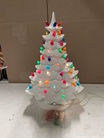 White ceramic Christmas tree with lit multicolor bulbs shown unlit environment