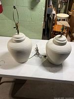 Pair of off-white ceramic table lamps on table, cords visible