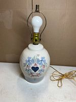 Front view of ceramic table lamp showing painted heart motif, bulb, harp and cord