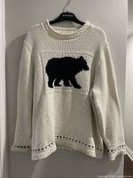 Front view of cream cotton sweater with black bear motif hanging on hanger