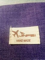 Close-up of JNFEI Hand Made fabric tag on purple canvas material