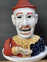 Front view of clown mechanical bank showing facial features, costume colours, lever arm