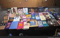 Overall lot of mixed paperback books laid out on workbench