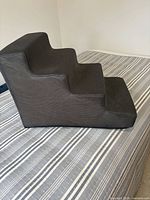Side view of grey three-step foam pet stairs on bed