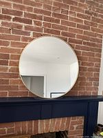 Front view of round gold metal framed mirror on brick wall