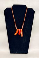 Full view of necklace on stand showing wooden beads and three coral branch pendants