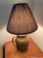 Tan ceramic jug lamp with pleated shade on wooden side table