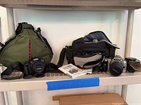 Both Canon cameras, two bags, manuals, extra lens and caps on shelf