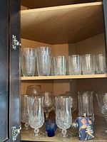 Cabinet view with highballs on top shelf, goblets, blue cordial and hip flask on lower shelf