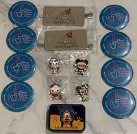 All items laid out: 8 buttons, 2 luggage tags, 4 sealed enamel pins, Pluto tin
