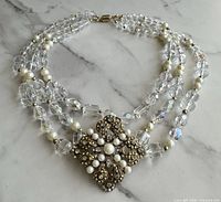 Full view of three-strand crystal and pearl necklace with ornate gold-tone pendant