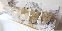 Four swan pieces lined up on marble surface with ruler for scale