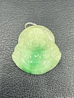 Front view of carved jadeite Laughing Buddha pendant showing coloration and jump ring
