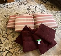 Group view of three pink striped bench cushions and four burgundy tufted chair pads