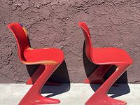 Side profile of both red Z-shaped chairs showing overall form and paint wear