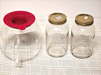 Group shot showing glass pitcher with red silicone strainer on top and two mason jars with lids