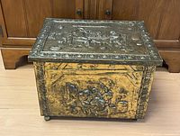 Front view of brass fireside box with embossed hearth scene and casters
