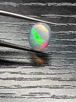 Opal held by tweezers showing bright green and red play-of-color