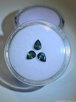 Three pear-cut blue-green sapphires in display case