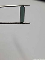 Gemstone held in tweezers side view showing long octagon profile and deep color