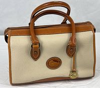 Front view of Dooney & Bourke satchel showing two-tone leather, handles, logo patch, brass fob