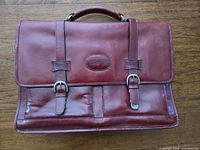 Front view of burgundy leather briefcase with buckle straps and top handle