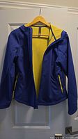 Front view of blue jacket on hanger showing hood, full zipper, yellow zip pockets