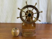 Full view of ship’s wheel on wooden stand with scale apple