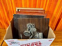 Box containing stacked wood plaques with metal car reliefs