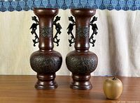Pair of bronze vases on table with apple for scale