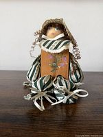 Front view of handmade wooden doll with striped dress and two matching shoe accessories