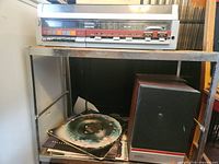 Full view of stereo main unit on shelf with speaker and stack of records