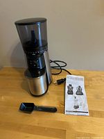 Grinder with scoop, manual and power cord displayed on tabletop