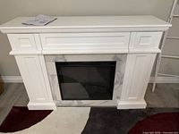 Front view of white electric fireplace mantel with marble-look surround