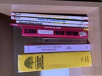 Stack of eight language and reference books on shelf showing spines and titles