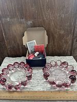 Pair of pink bubble-rim ashtrays and boxed Forever Lamp on lace cloth with ruler for scale