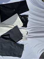 Four folded pairs of pants in black, off-white and grey displayed on sheet