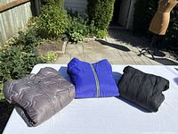 Three folded jackets: grey, royal blue, black displayed on table