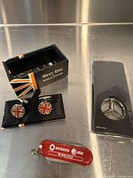 All three items: cufflinks in box, keychain multi-tool, Mercedes emblem in package