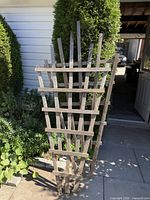 stack of three wooden garden trellises leaning against shrub