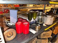 Lot overview showing candles, goblets, lantern, rattan holder, finial on shelf
