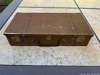 Front and top view of brown suitcase-style tin showing handle and latch graphics